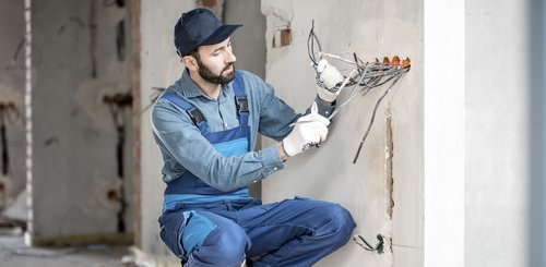 Ein Elektroniker der auf einem Rohbau die Kabel aus der Wand zieht