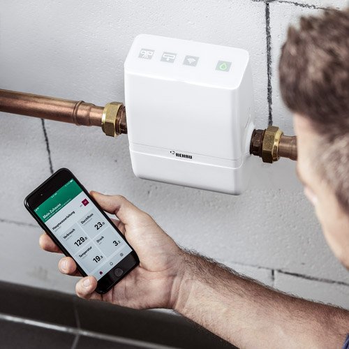 Eine Wassersteuerung und ein Mann der eine App auf dem Smartphone bedient